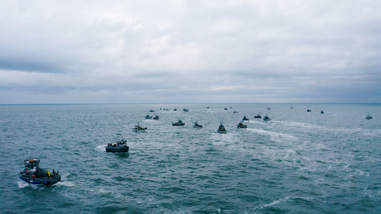 Multiple boats scattered across a large body of water under an overcast sky.